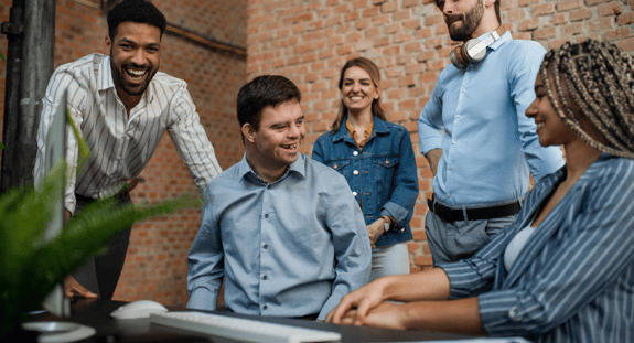 Making Digital Learning More Inclusive & Accessible - a diverse group of people sit and stand around a desk smiling