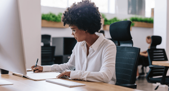 Online Learning The Ultimate Guide 2023  - Woman sits at desk writing on paper with computer in front of her